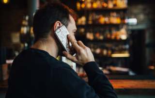 kaboompics Handsome young man with smartphone drinking whisky at bar or pub